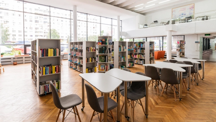 Bright modern library interior with bookshelves, tables, and seating designed for collaborative learning and study.